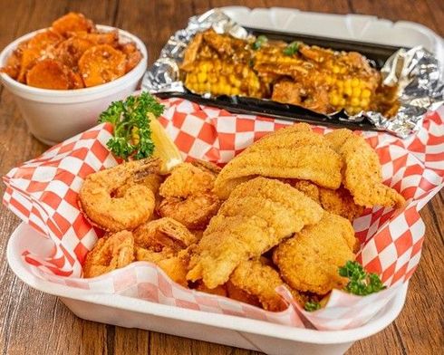 A plastic container filled with fried shrimp and fish on a wooden table.