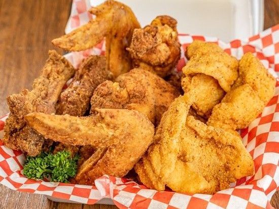 A basket of fried chicken and fish on a checkered paper on a table.