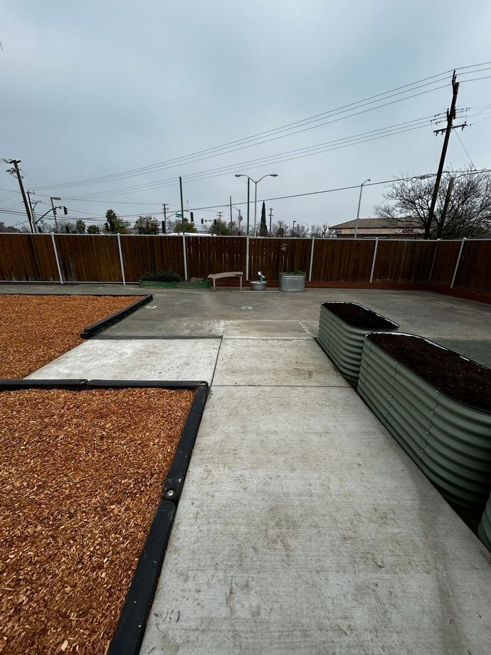 Concrete backyard patio with gravel beds, corrugated planter, and wooden fence under cloudy sky