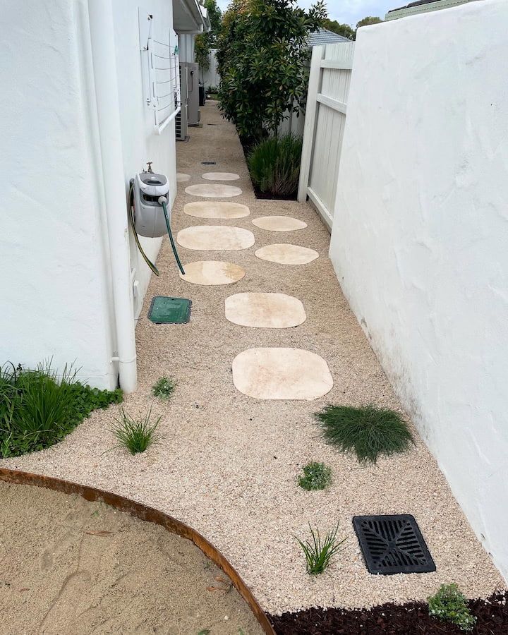 Stone path with stepping stones, gravel, white walls, and small plants in a narrow outdoor space.