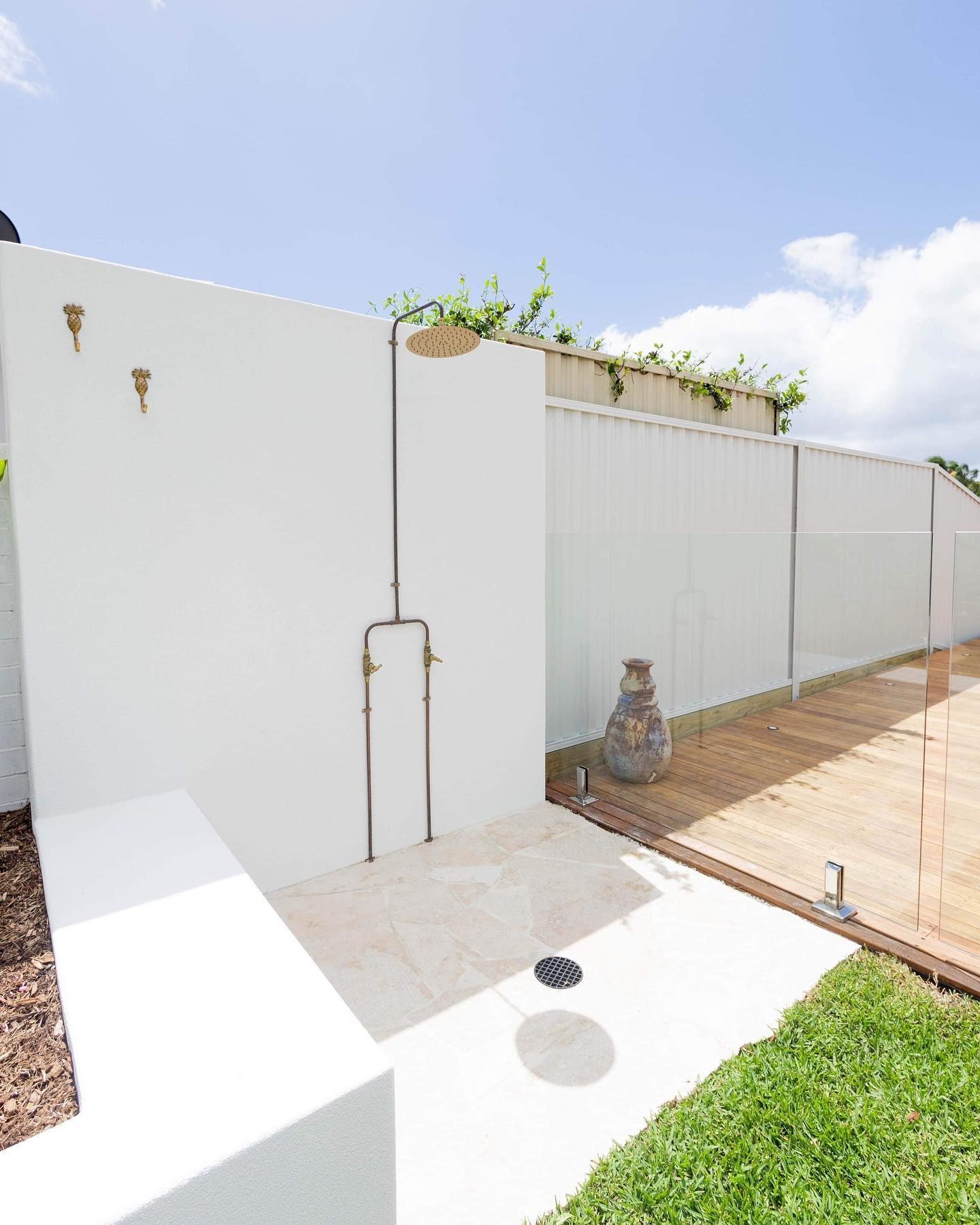 Outdoor shower with white walls, metal fixtures, and wooden deck.