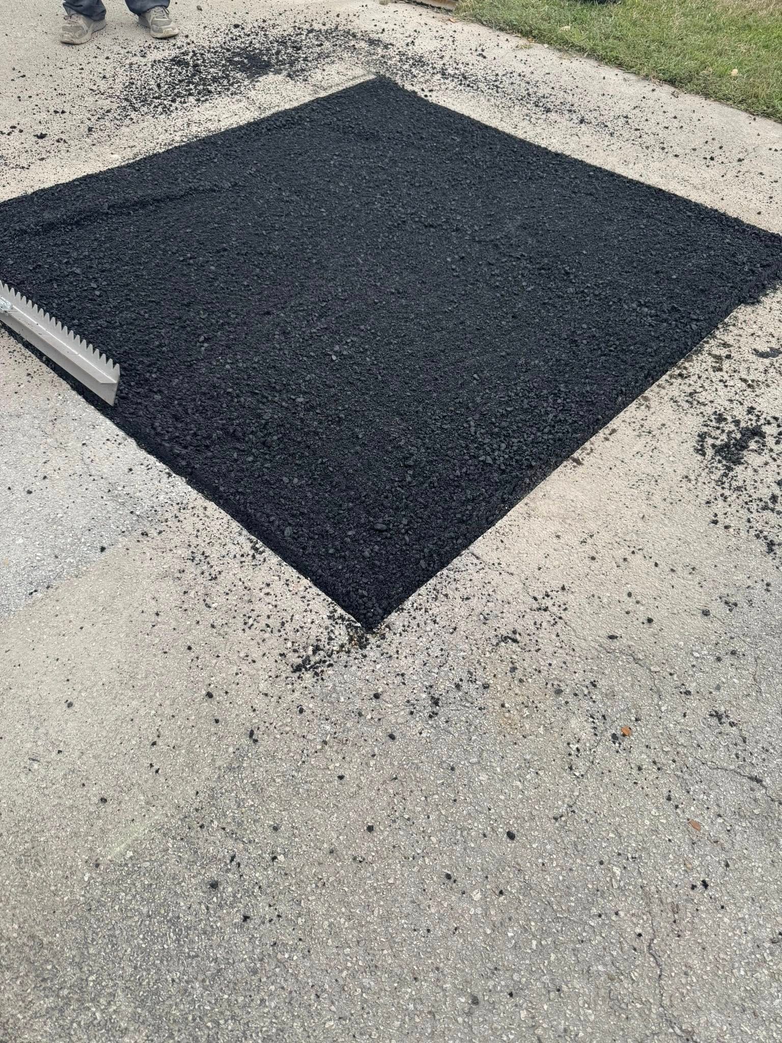 Black square patch on a speckled concrete surface, bordered by white painted lines.