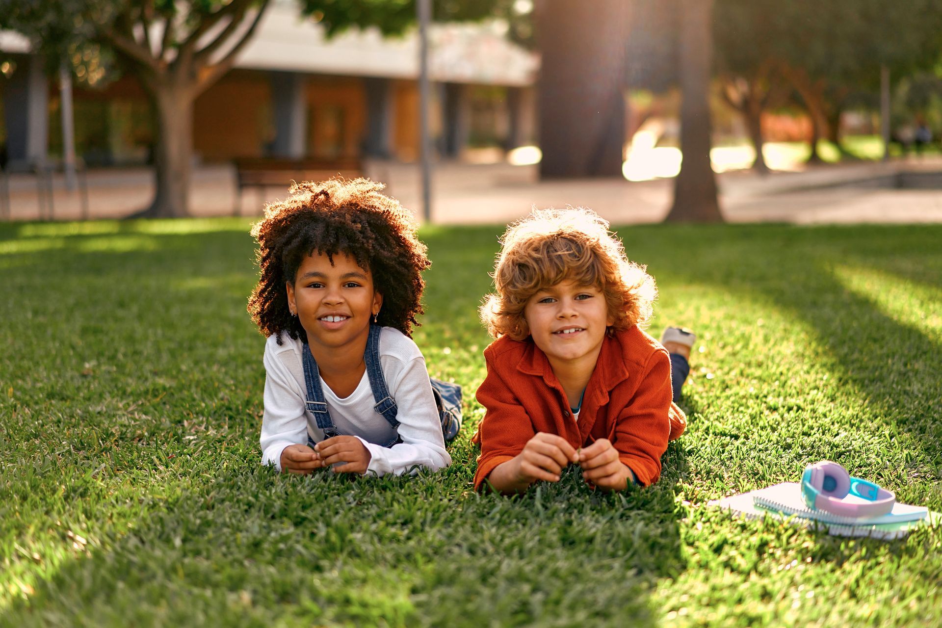 Two young boys are laying on the grass in a park.