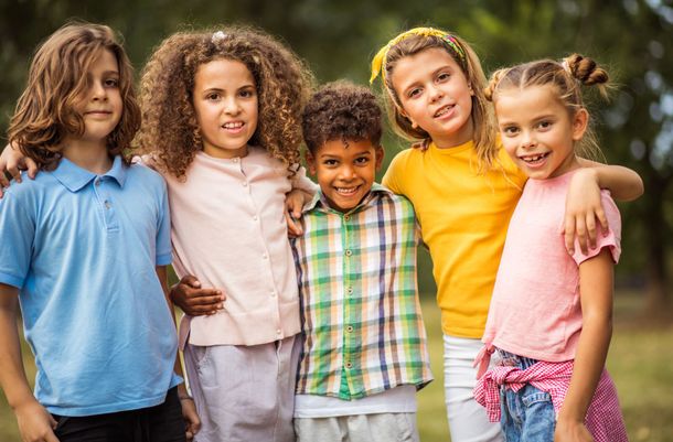 Group of five children smiling, arm in arm, outdoors.