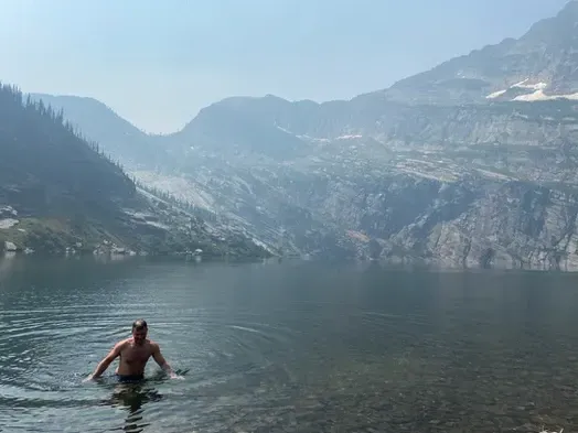 A man is swimming in a lake with mountains in the background.