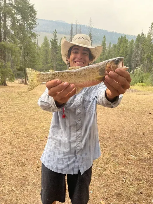 A man in a cowboy hat is holding a fish in his hands.