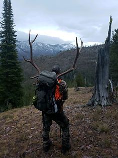A man with a backpack and antlers is standing on top of a hill.