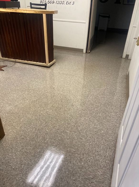 Shiny, speckled floor in an office with a dark wooden counter. White walls and a doorway are visible.