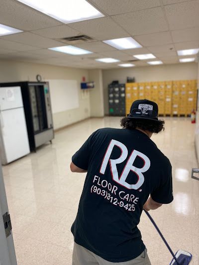 Person mopping a hallway in a room with lockers, wearing a black RB Floor Care shirt.
