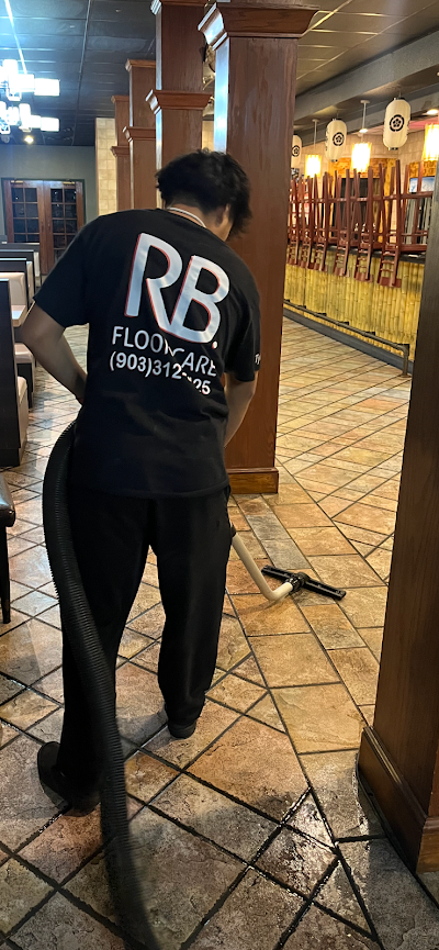Person in a black RB sweatshirt sweeping a tiled corridor inside a warmly lit venue.