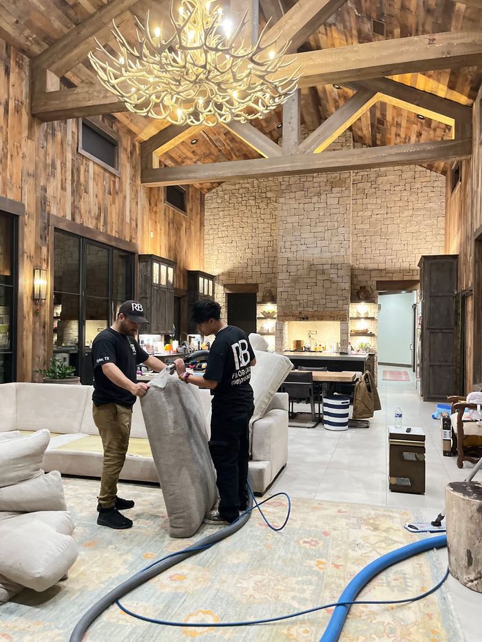 Two men are cleaning a couch in a living room.