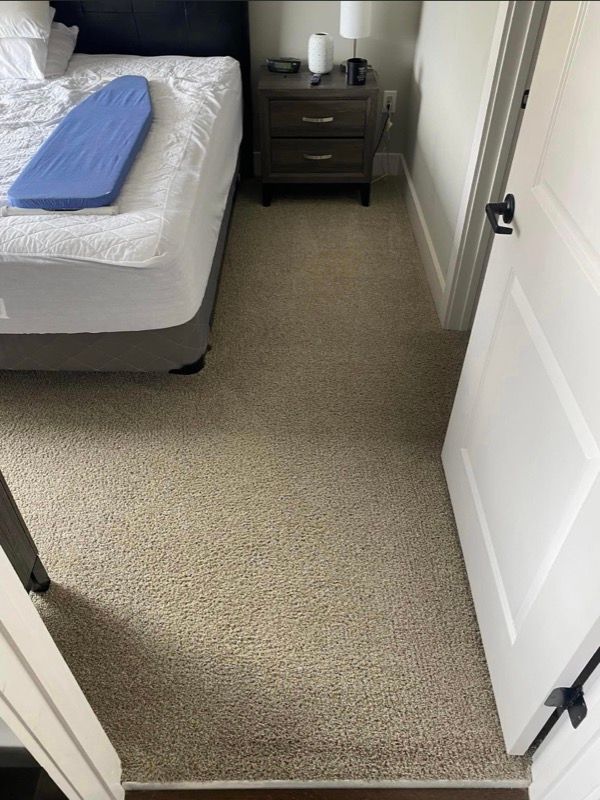 Bedroom with a bed, nightstand, carpet, and open white door.