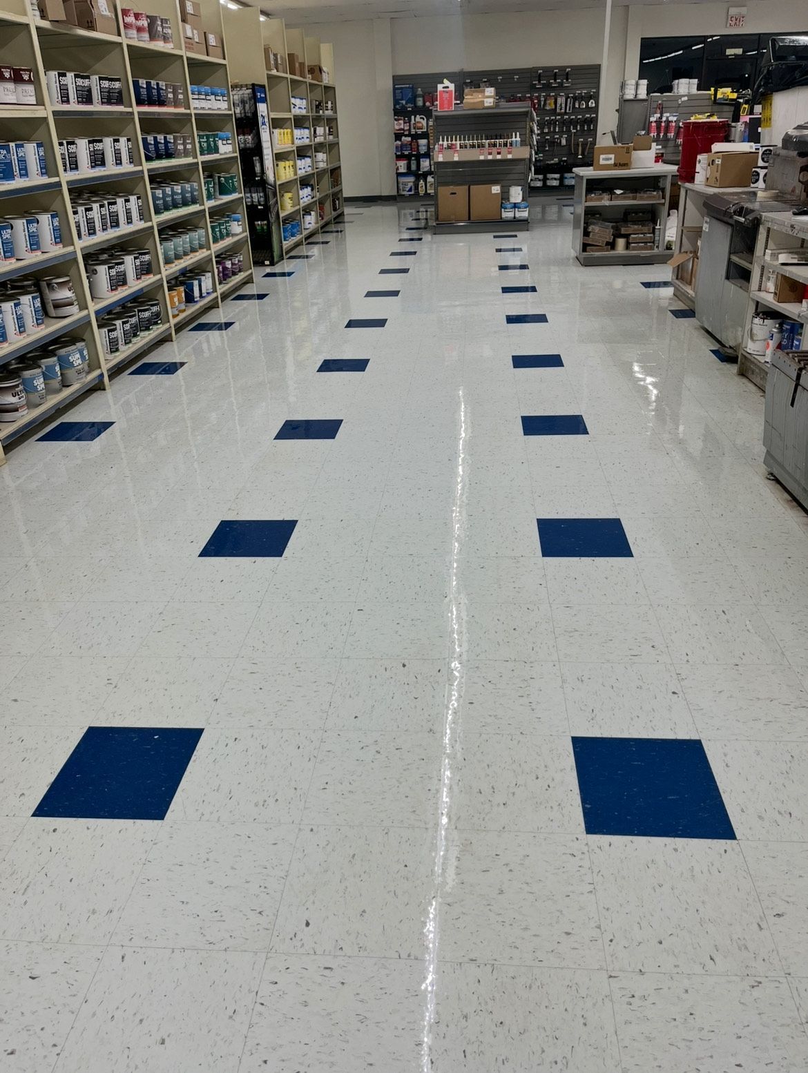 Store aisle with blue floor markers and shelves on both sides, viewed from the center.