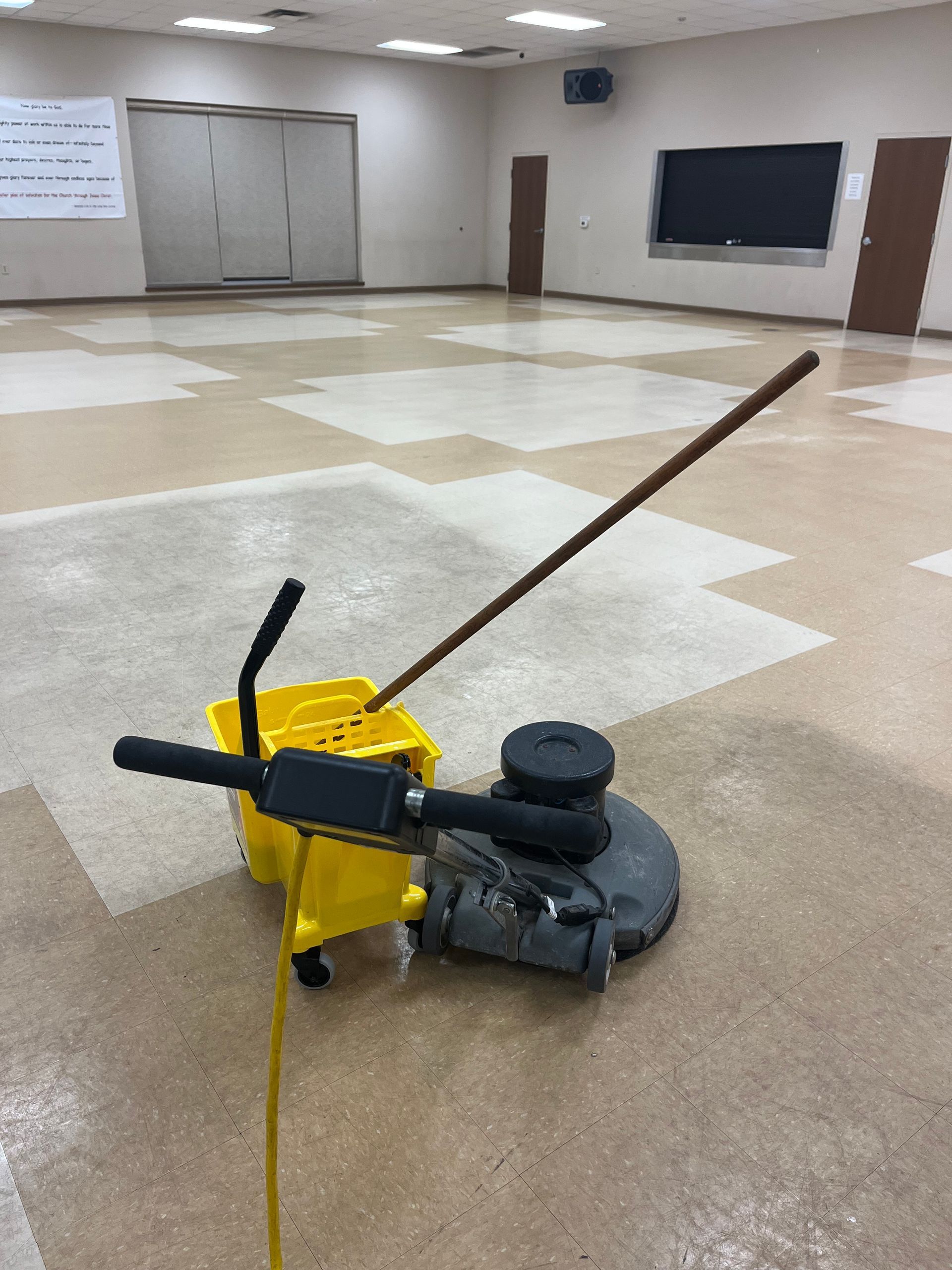 Yellow floor cleaning machine and bucket in a large, empty room with checkered tile flooring.