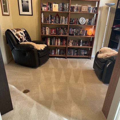 A cozy reading nook with two recliners, bookshelves, and a lamp on a light beige carpet.