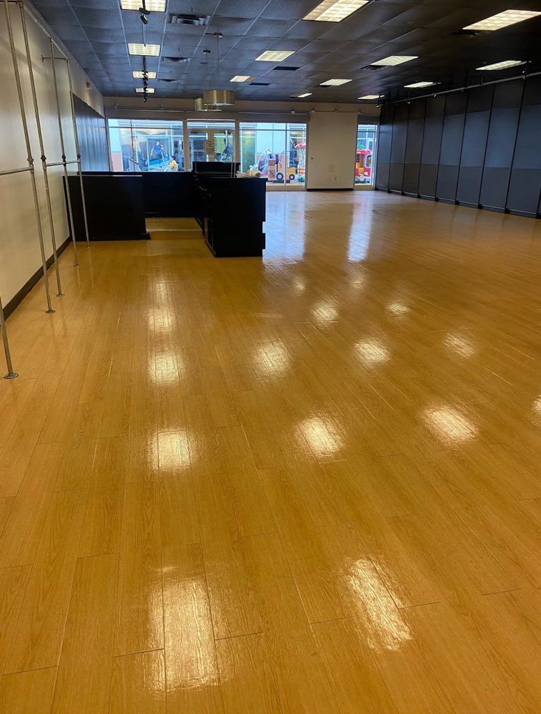 Empty commercial space with shiny, wood-like floors; a black counter.
