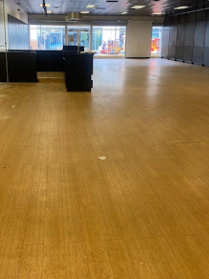 Empty commercial space with wooden floor, large windows, and dark storage units.