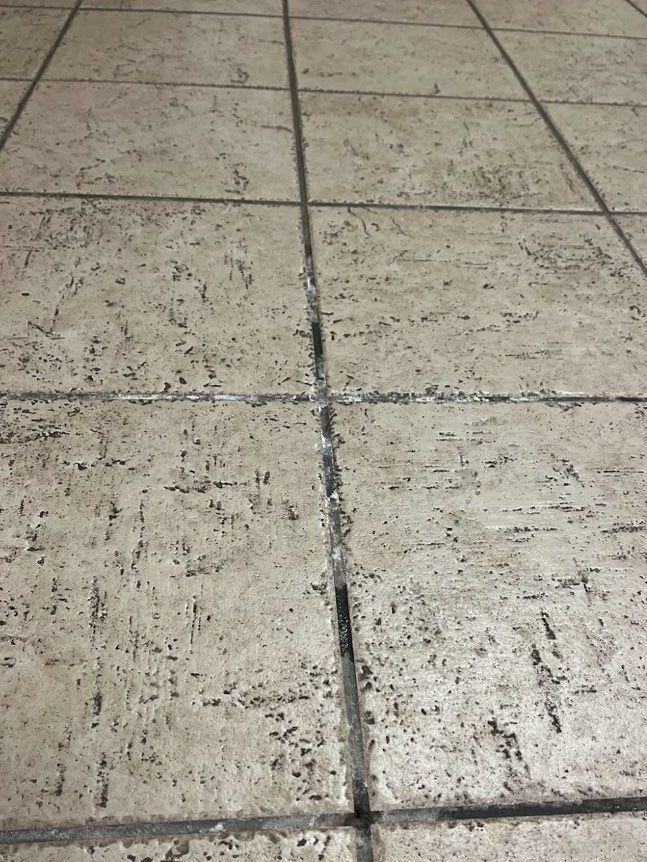 Close-up of off-white floor tiles with dark grout lines, showing wear and tear.