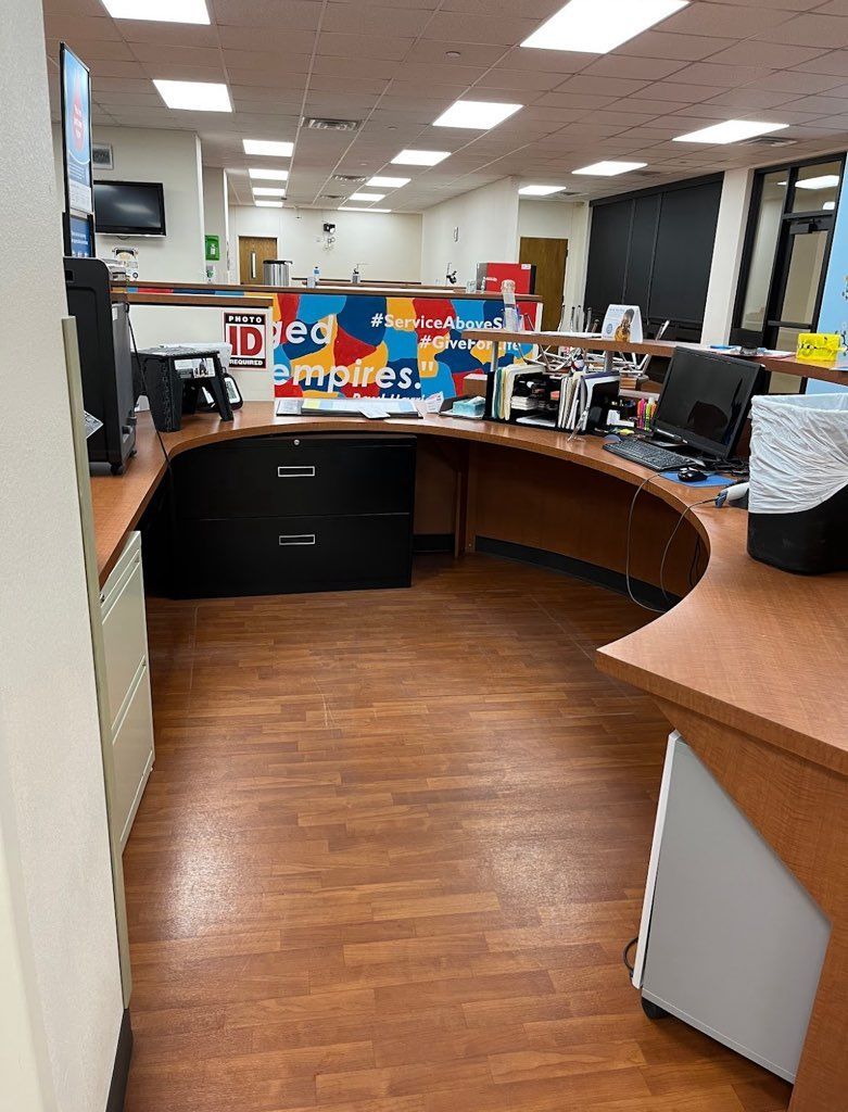 Reception desk in a medical office, brown countertop and cabinets, wood floor, colorful artwork in the background.