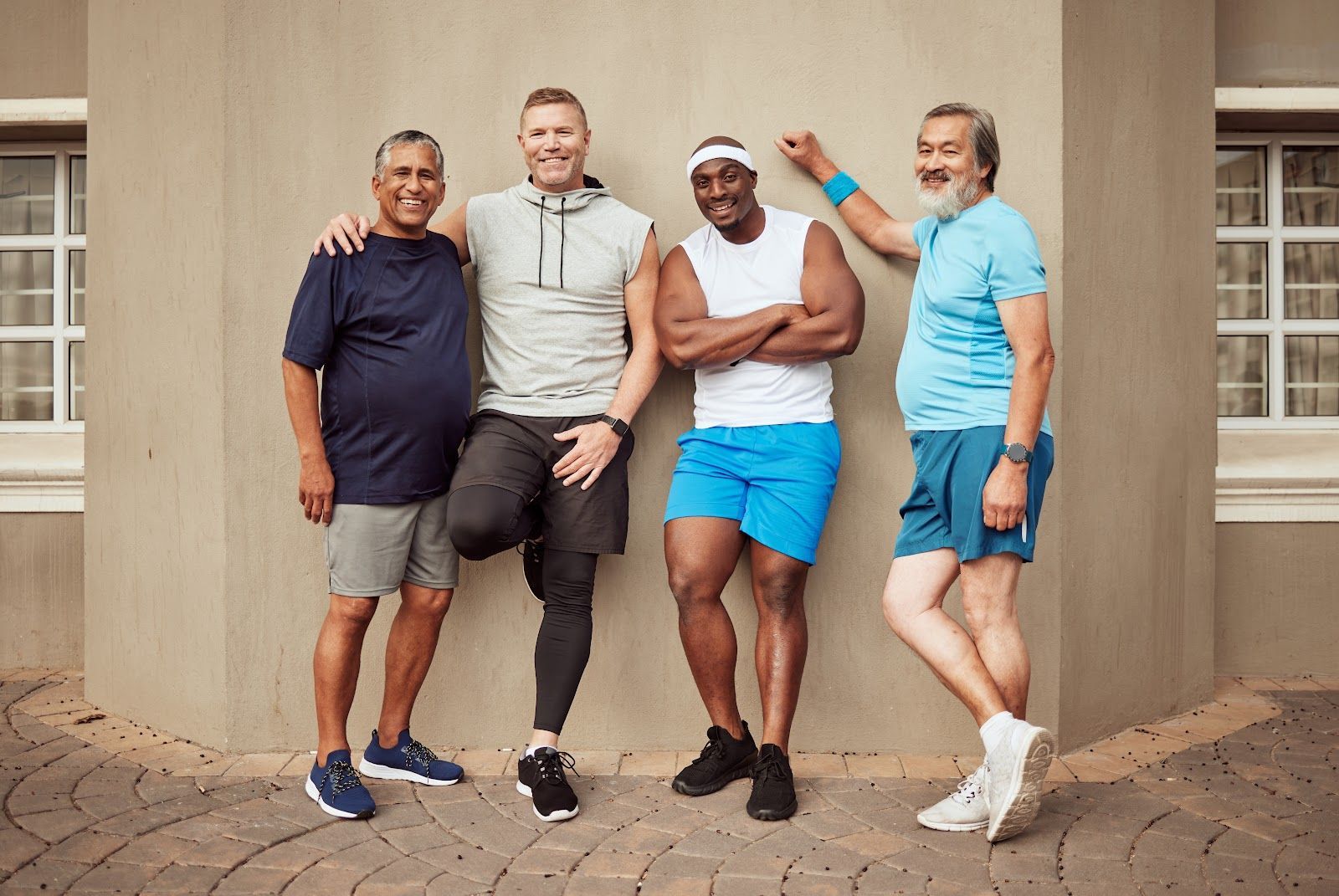Four friends pose together outdoors against a beige wall, smiling and leaning casually.