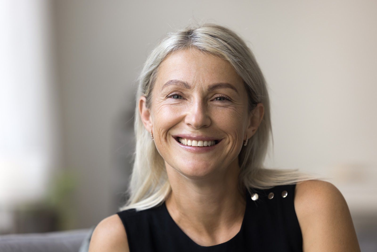Smiling person with long gray hair wearing a black sleeveless top against a blurred background