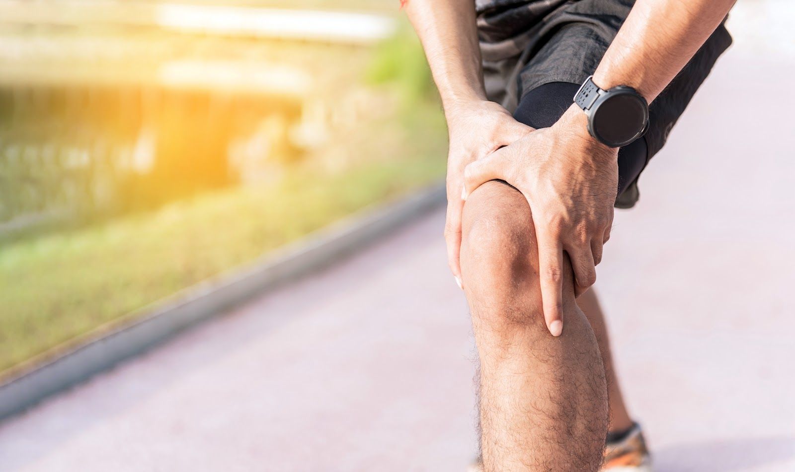 Runner holding an injured knee on a track, with a smartwatch on wrist and blurred motion in the background