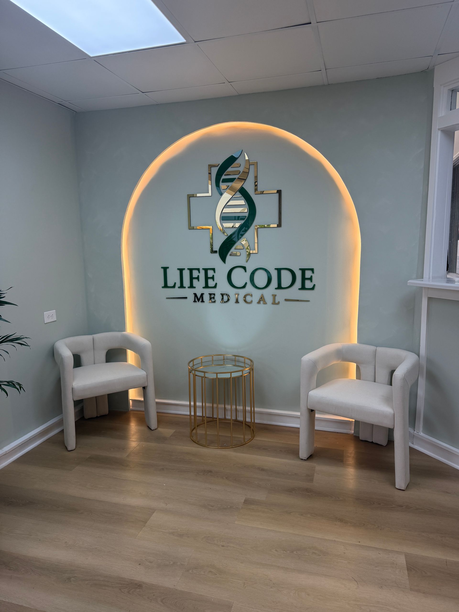 Reception nook with Life Code Medical logo, two white chairs, and a small gold table under warm arch lighting