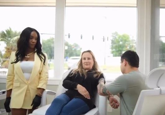 Three people talking in a bright waiting room with large windows.