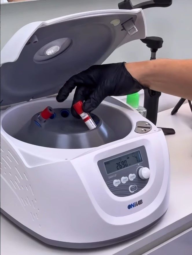 Gloved hand places red-topped tubes into a laboratory centrifuge with lid open.