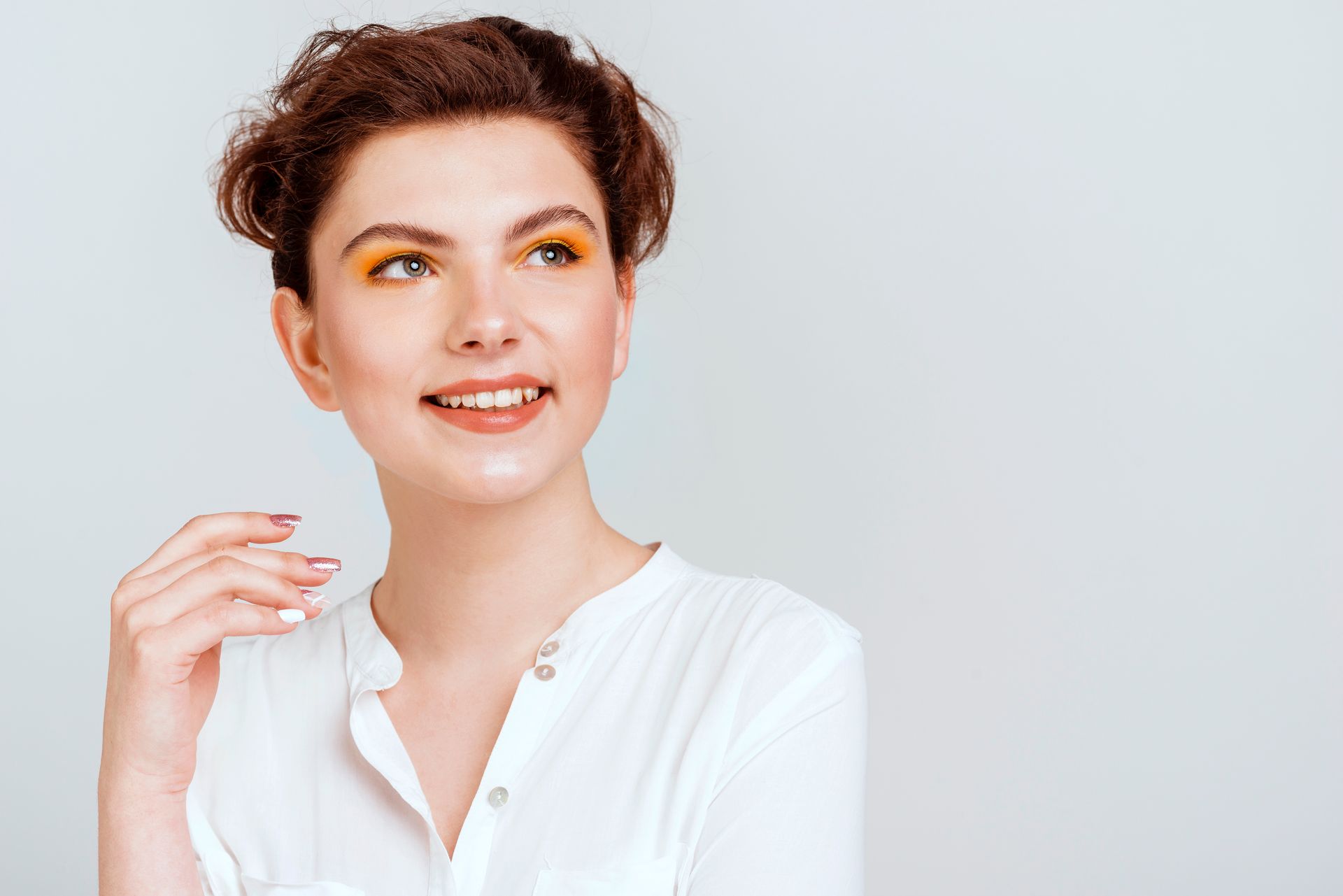 Smiling person in a white blouse with short curly hair, looking off to the side against a light background