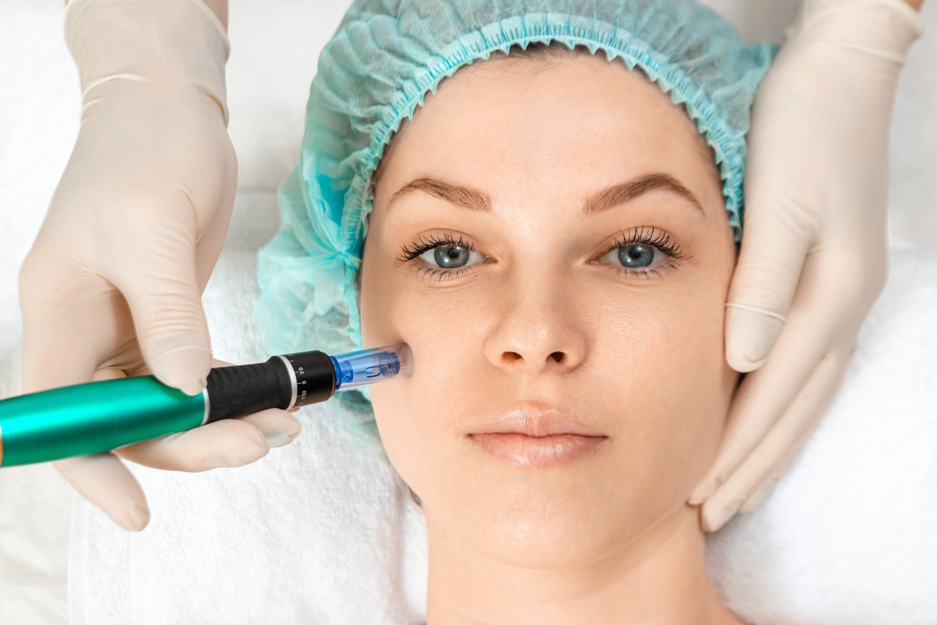 Cosmetic treatment with gloved hands using a handheld device on a woman's face