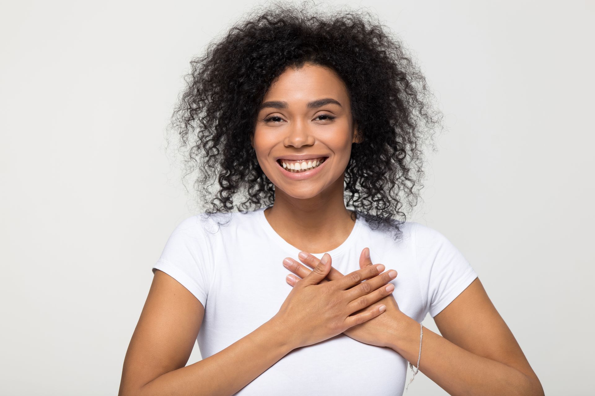 Smiling woman in a white shirt with hands on her chest against a light background