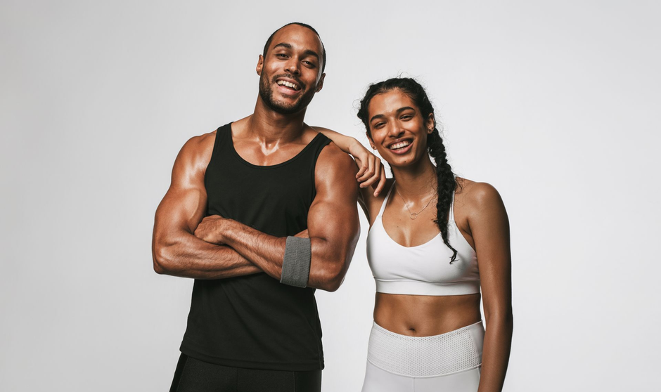 Two smiling fitness models in workout clothes standing against a gray background