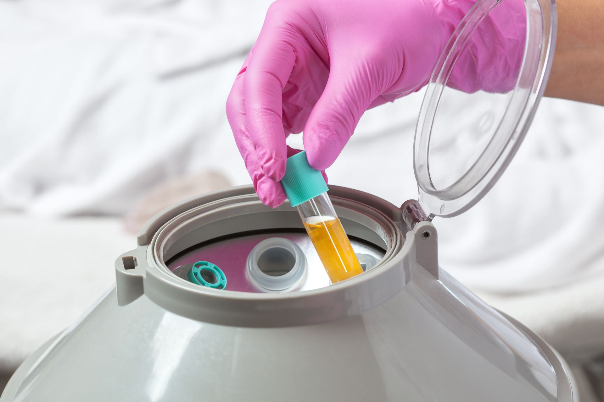Gloved hand placing a test tube into a lab centrifuge with the lid open