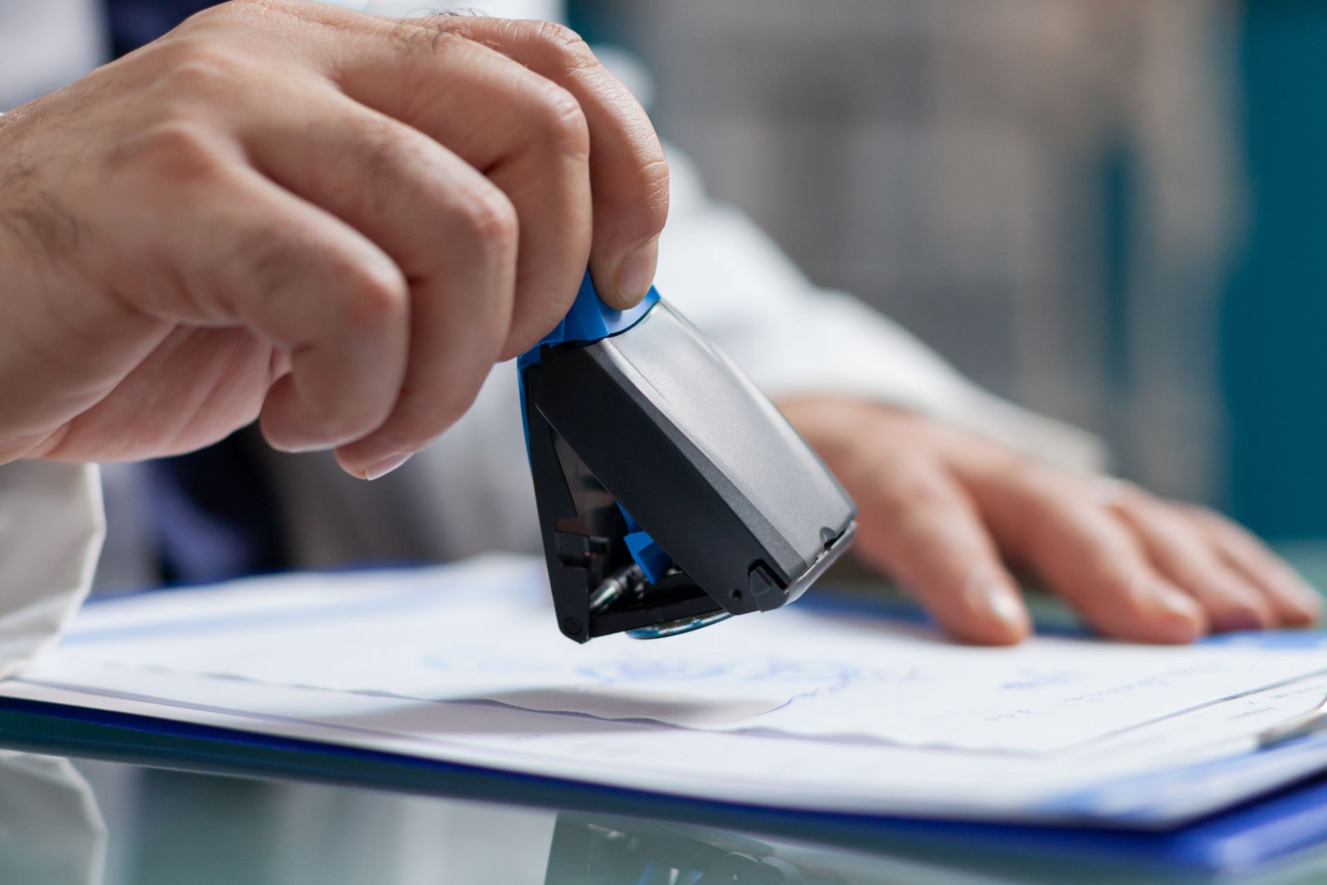 Hand stamping documents on a desk with a blue rubber stamp