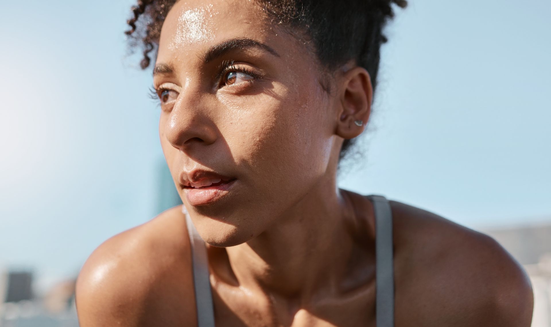 Sweaty athlete resting outdoors under bright sunlight, gazing to the side