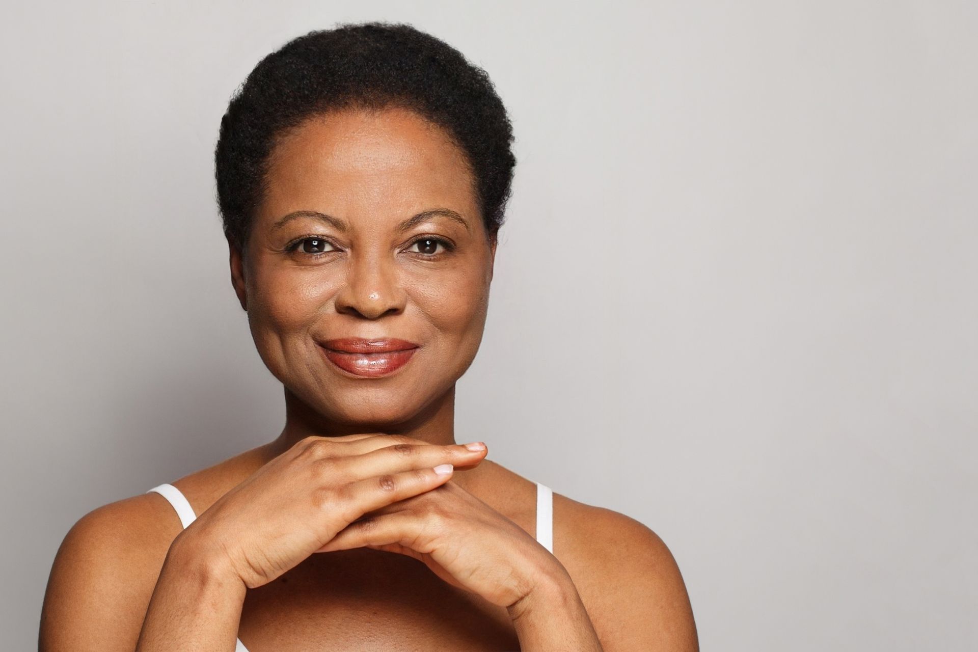 Smiling woman with short hair resting her chin on her hands against a gray background