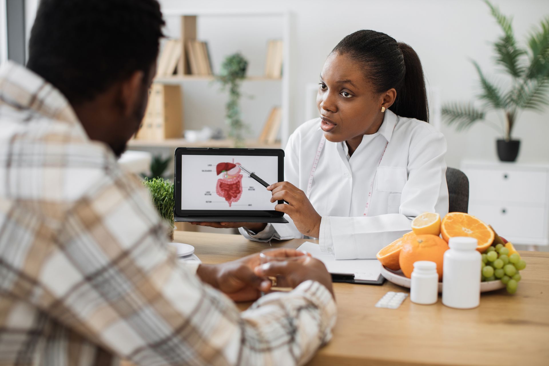 Doctor explaining a heart scan on a laptop to a patient in a clinic, with oranges and pill bottles on the table