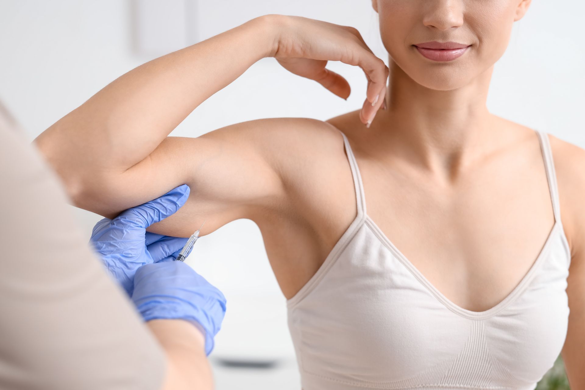 Person with raised arm receiving an injection in the upper arm from a healthcare worker wearing blue gloves
