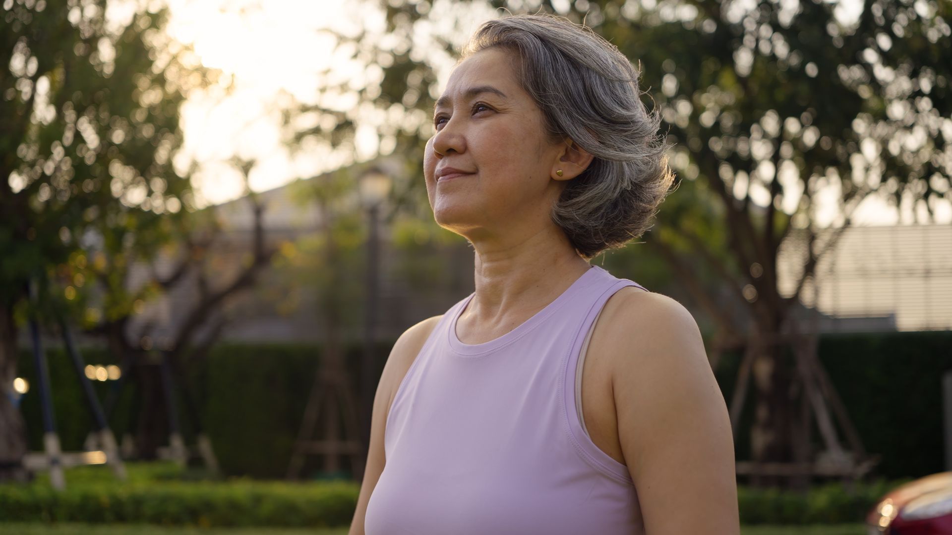 Woman in a light pink sleeveless top standing outdoors at sunset, looking upward and smiling.