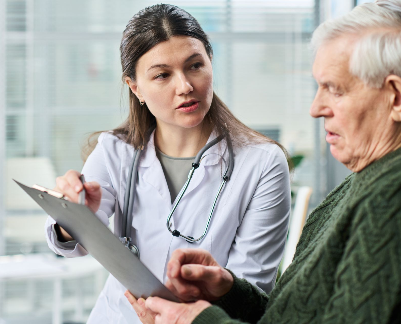 Doctor reviewing a clipboard with an older man in a green sweater during a consultation