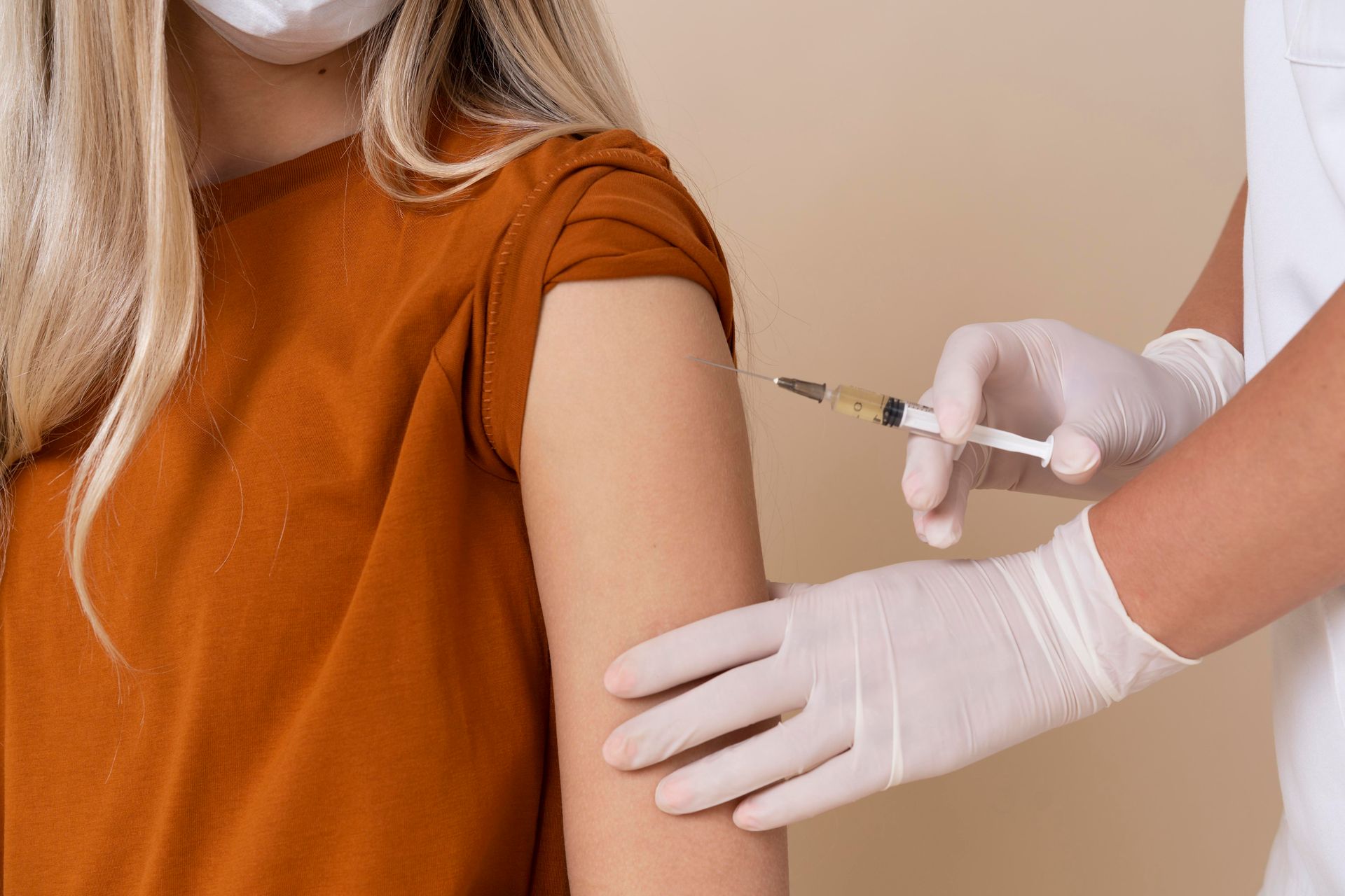 Gloved clinician giving a shoulder injection to a person in an orange shirt