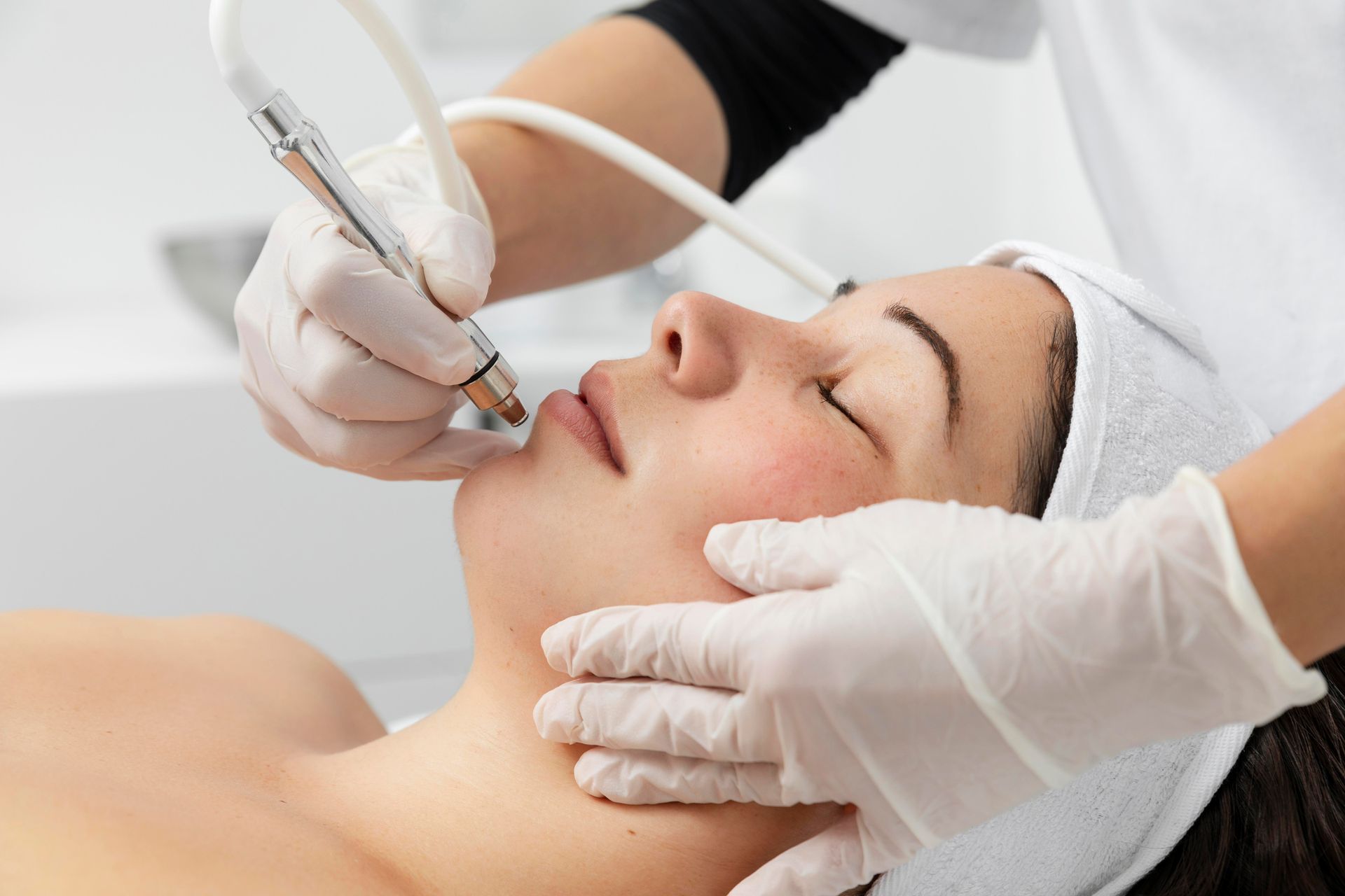 Aesthetic facial treatment with gloved hands using a handheld device on a relaxed client