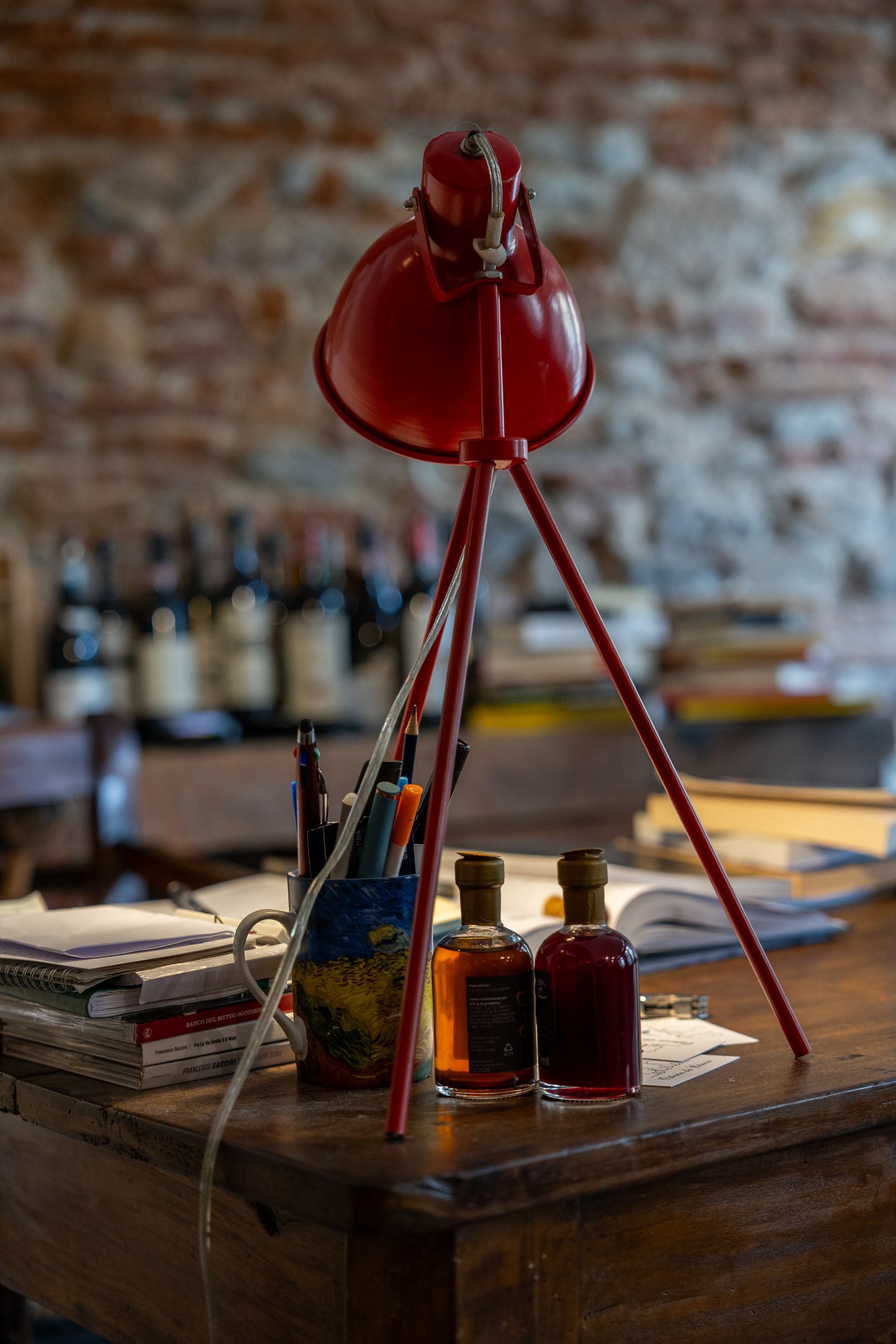 Una lampada da scrivania rossa sopra un tavolo di legno rustico con boccette d'inchiostro e fogli di carta in un'accogliente stanza con pareti in mattoni.
