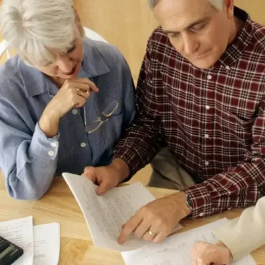 Two people reviewing documents at a table, pointing at a page with a calculator nearby.