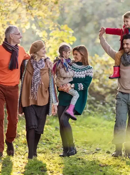 Five people walking together in a sunny autumn park, with two children being carried.