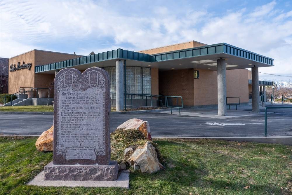 Stone monument in front of a brick building with a covered entrance and grassy lawn.