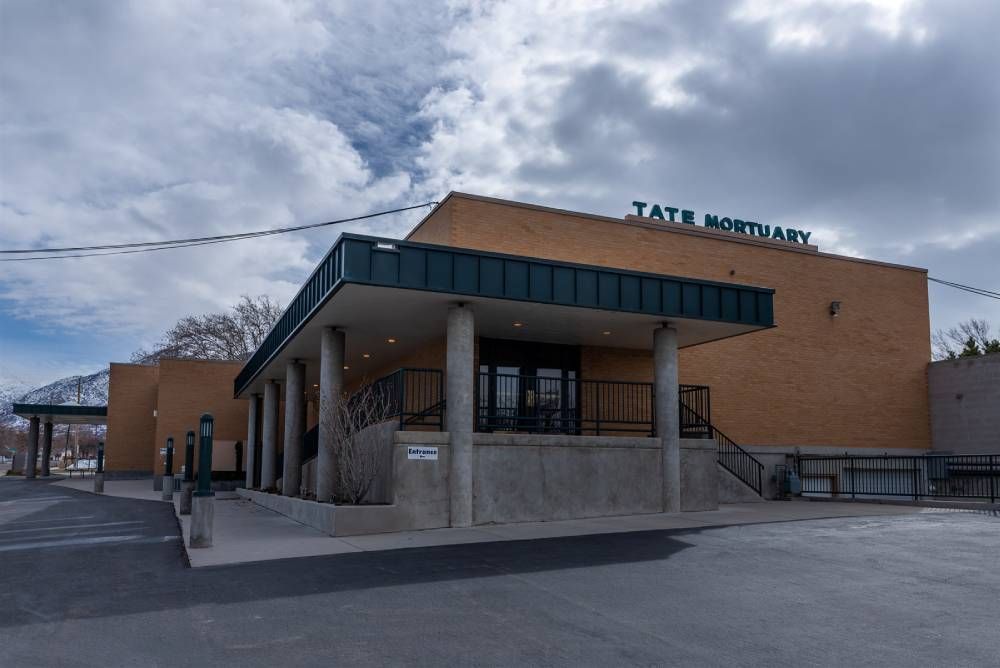 Exterior of Tate Mortuary, a brick building with a covered entrance under a cloudy sky.
