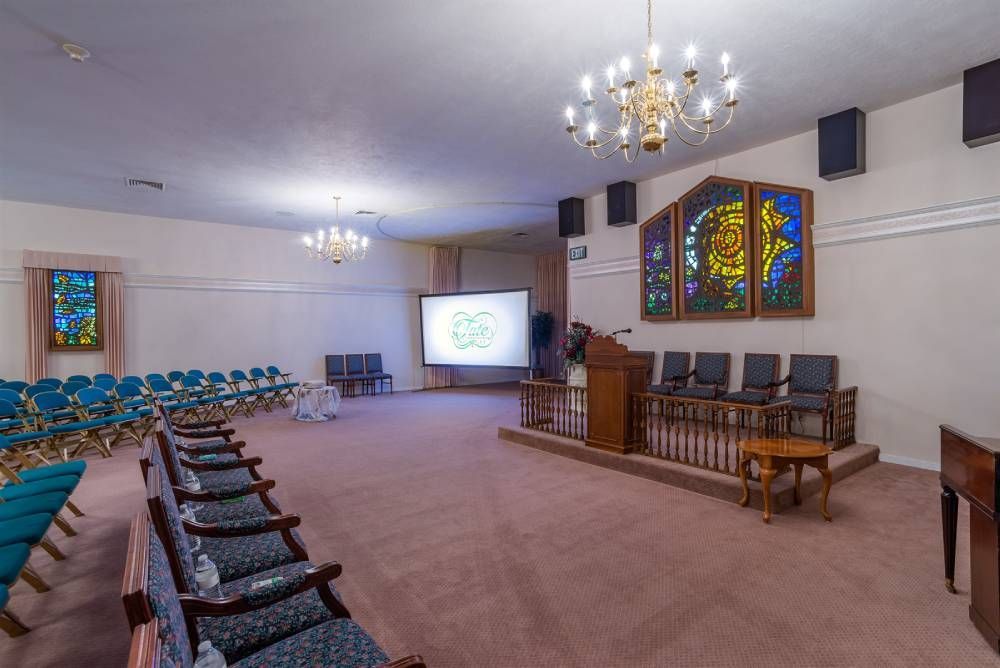 Empty church sanctuary with rows of teal chairs, stained glass windows, and a pulpit at the front