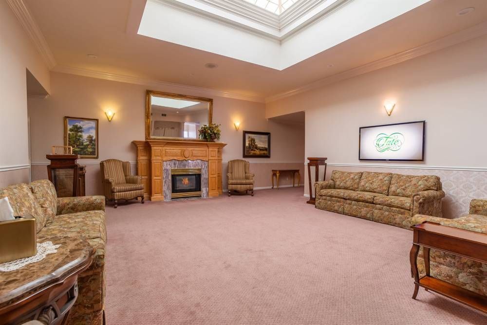Spacious beige living room with fireplace, skylight, and patterned sofas around a central carpeted seating area.